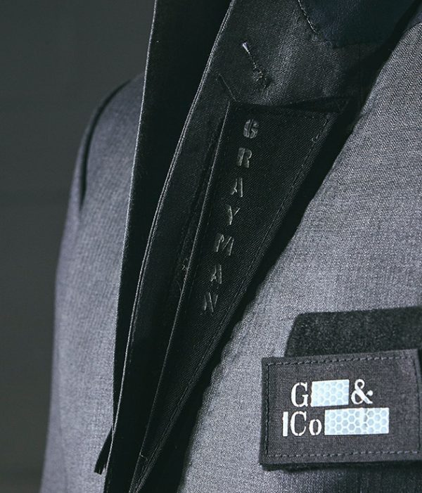 Angled close-up frontal shot of Grayman and Company branded velcro lapels sitting on a grey herringbone suit jacket