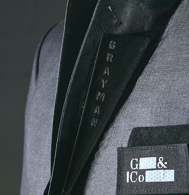 Angled close-up frontal shot of Grayman and Company branded velcro lapels sitting on a grey herringbone suit jacket