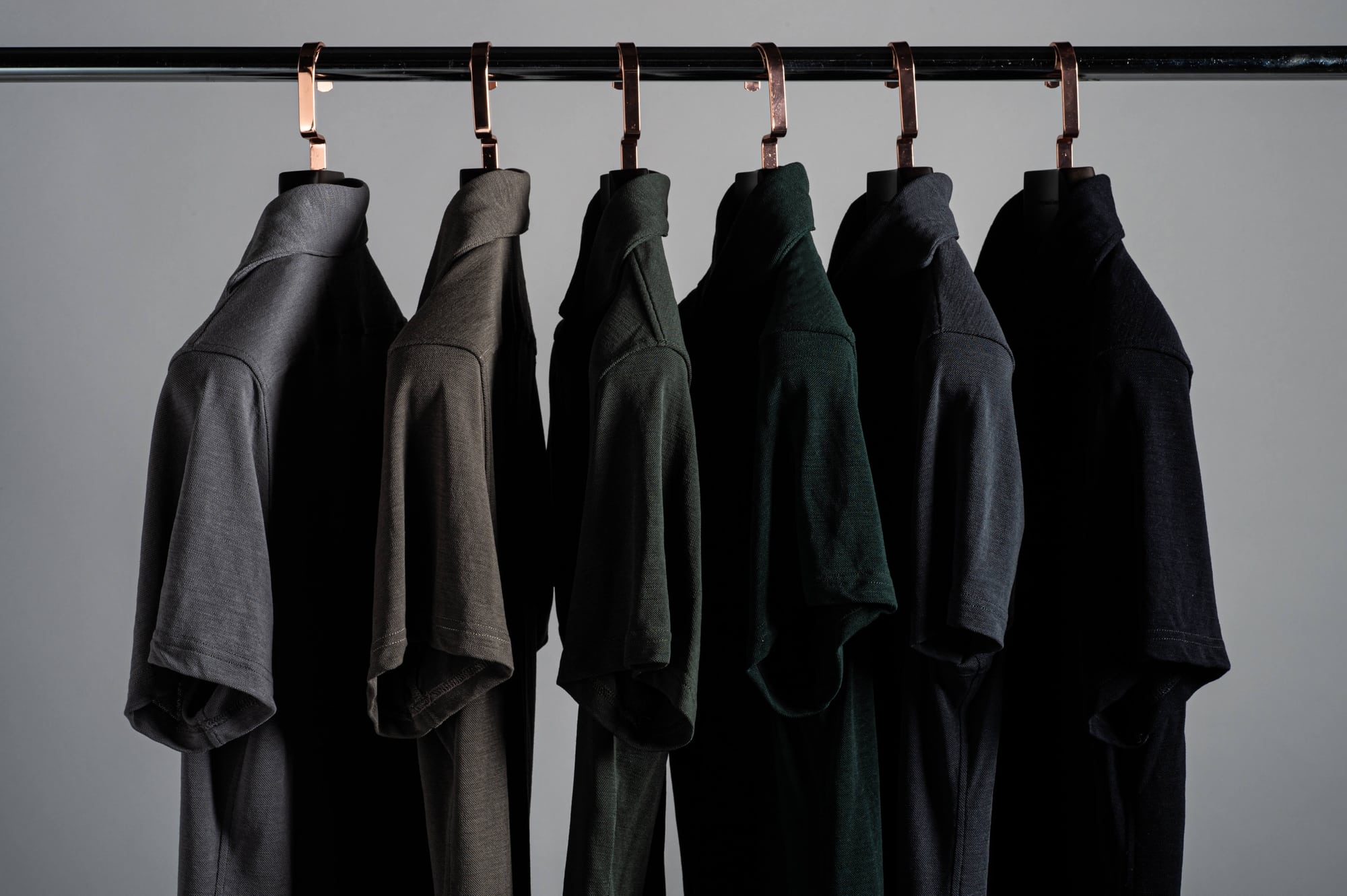 Rack of Grayman and Company pique merino polo shirts on a colour gradient against a gray background with thick luxury hangers