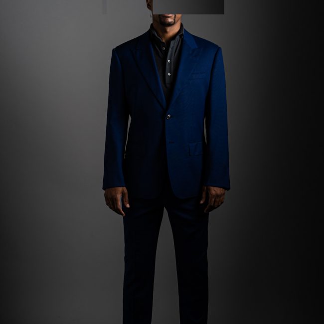 redacted man in studio wearing grey merino pique polo shirt and blue tactical suit by Grayman and Company with grey backdrop