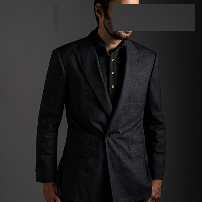 redacted man in studio wearing green merino pique polo shirt and tactical suit by Grayman and Company with grey backdrop