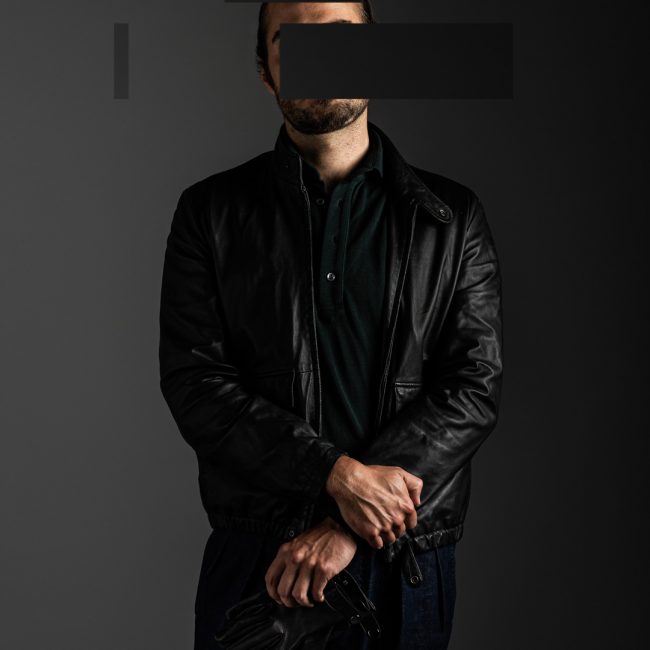 redacted man in studio wearing green merino pique polo shirt and black leather jacket by Grayman and Company with grey backdrop