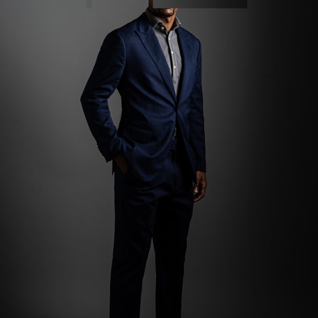 redacted man in studio wearing light grey merino pique polo shirt and tactical blue suit by Grayman and Company with grey backdrop