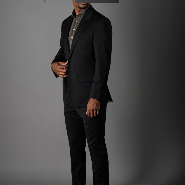Model wearing Grayman and Company taupe pique polo with Loro Piana tic weave grey 662049 single breasted peak lapel suit against grey background with redacted face